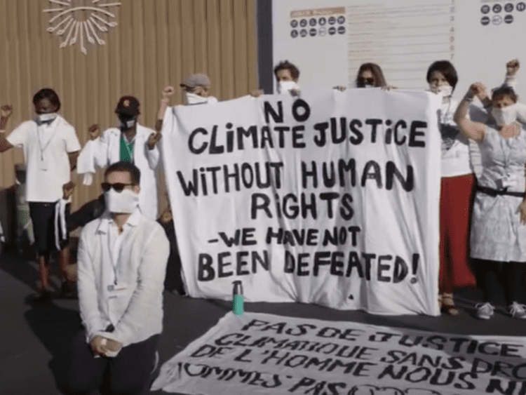 Climate protesters at COP27 with a banner that reads: No climate justice without human rights. We have not been defeated!